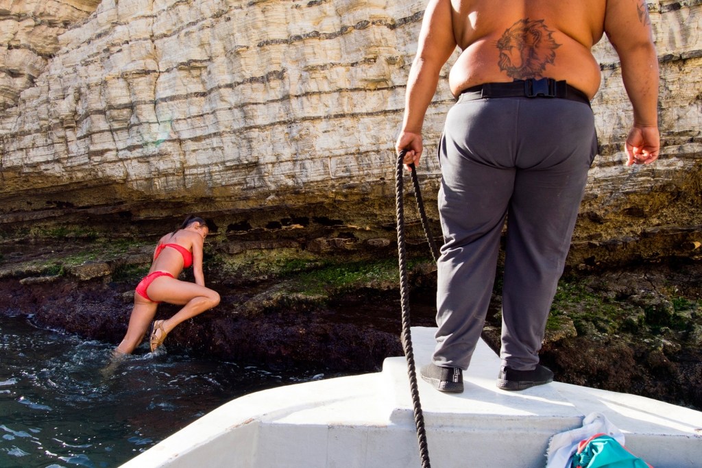 A girl in red swimsuit trying to climb over the Raouche Rock in Beirut, Lebanon  (Roï Saade / Gulf Photo Plus)