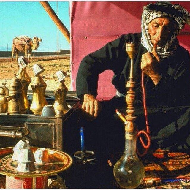 A guy sitting in the tent and smoking Narghile (Shisha) . You can see the Arabic coffee one of Baalbeck traditions served while welcoming guests, back you can see also the camel used before transportation.