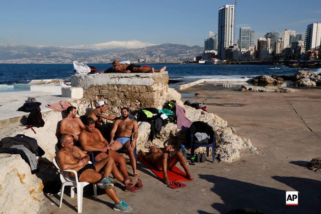 Men sunbathing by the Mediterranean sea, as snow is seen on the background covering the mountains, in Beirut, Lebanon